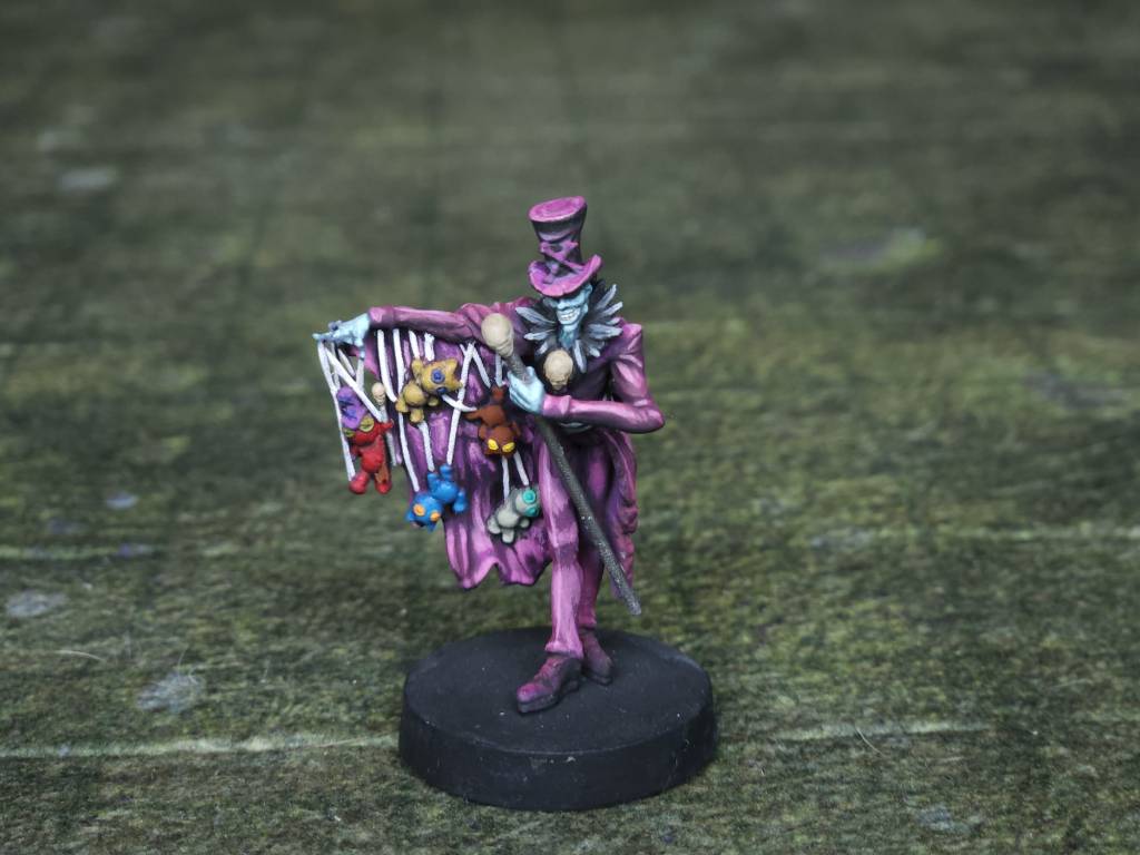 An image of a miniature man in a purple top hat opening his coat to reveal puppets hanging on string.